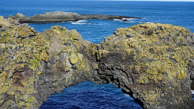 Scenic view of natural rock arch formation over the ocean in Iceland, vibrant blue waters.
