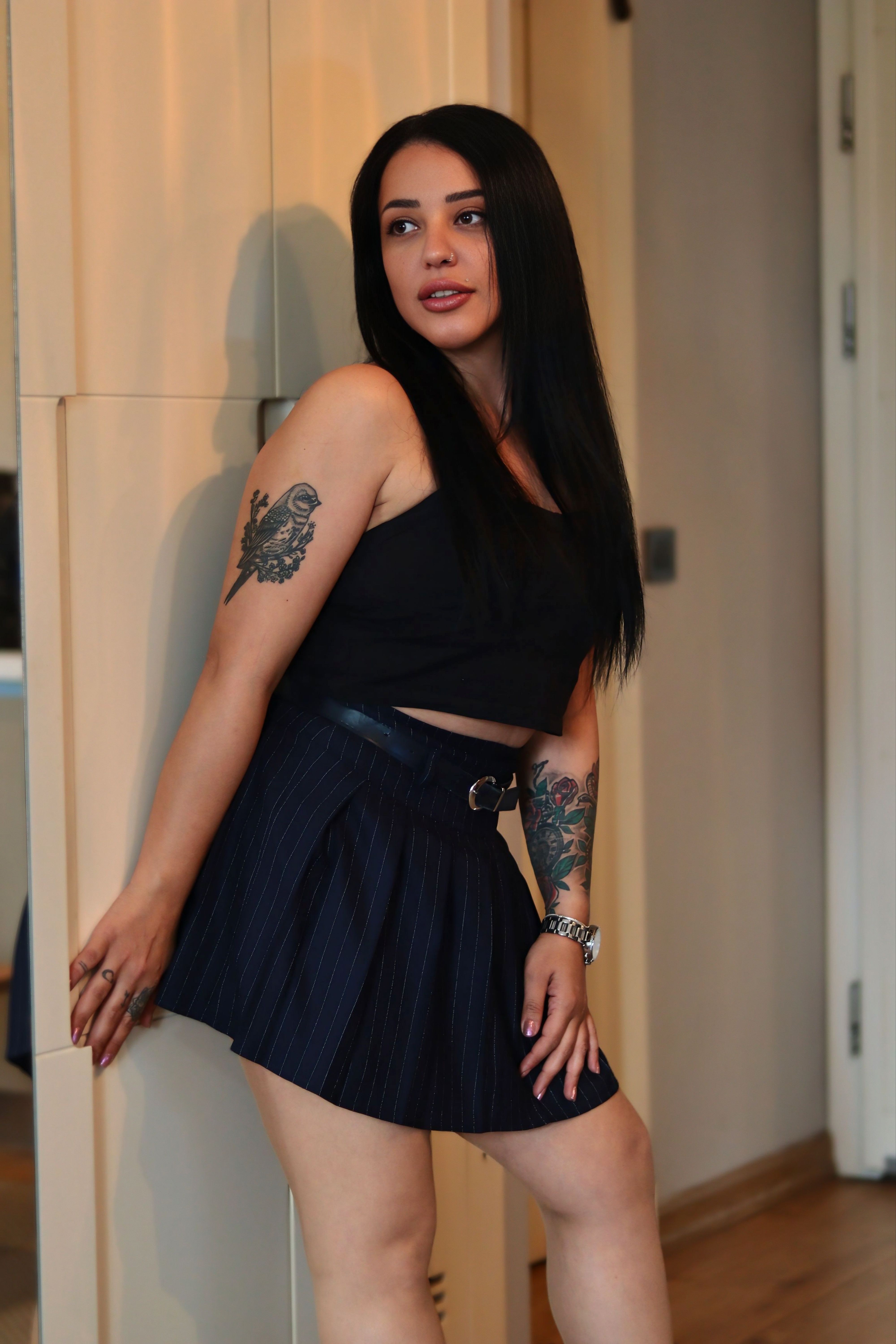 Elegant woman with tattoos posing indoors in stylish attire.