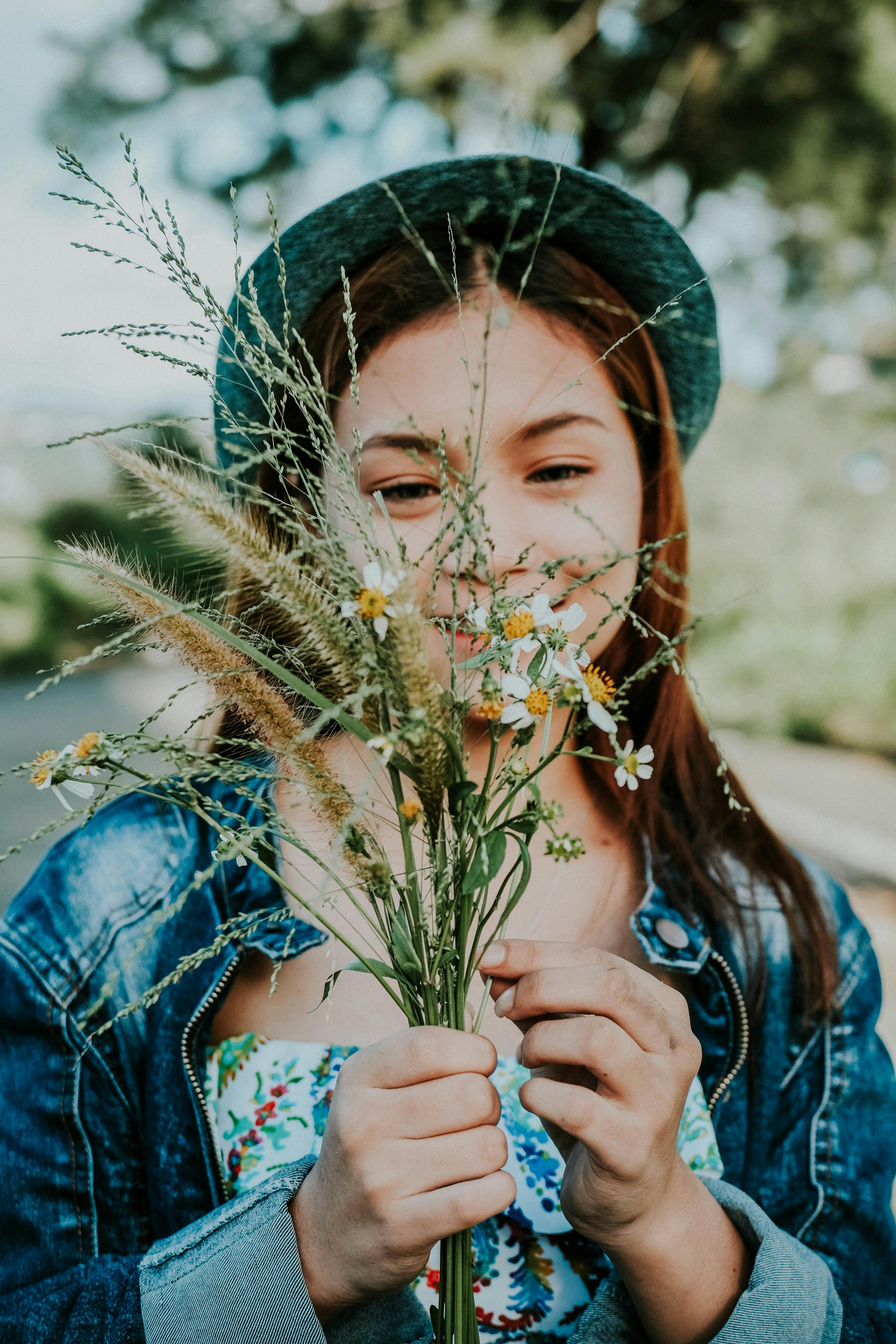 一名穿着牛仔夹克的年轻女子在户外微笑着手拿野花，时尚与自然完美融合