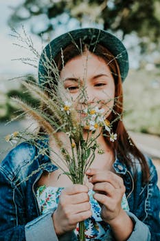 一名穿着牛仔夹克的年轻女子在户外微笑着手拿野花，时尚与自然完美融合