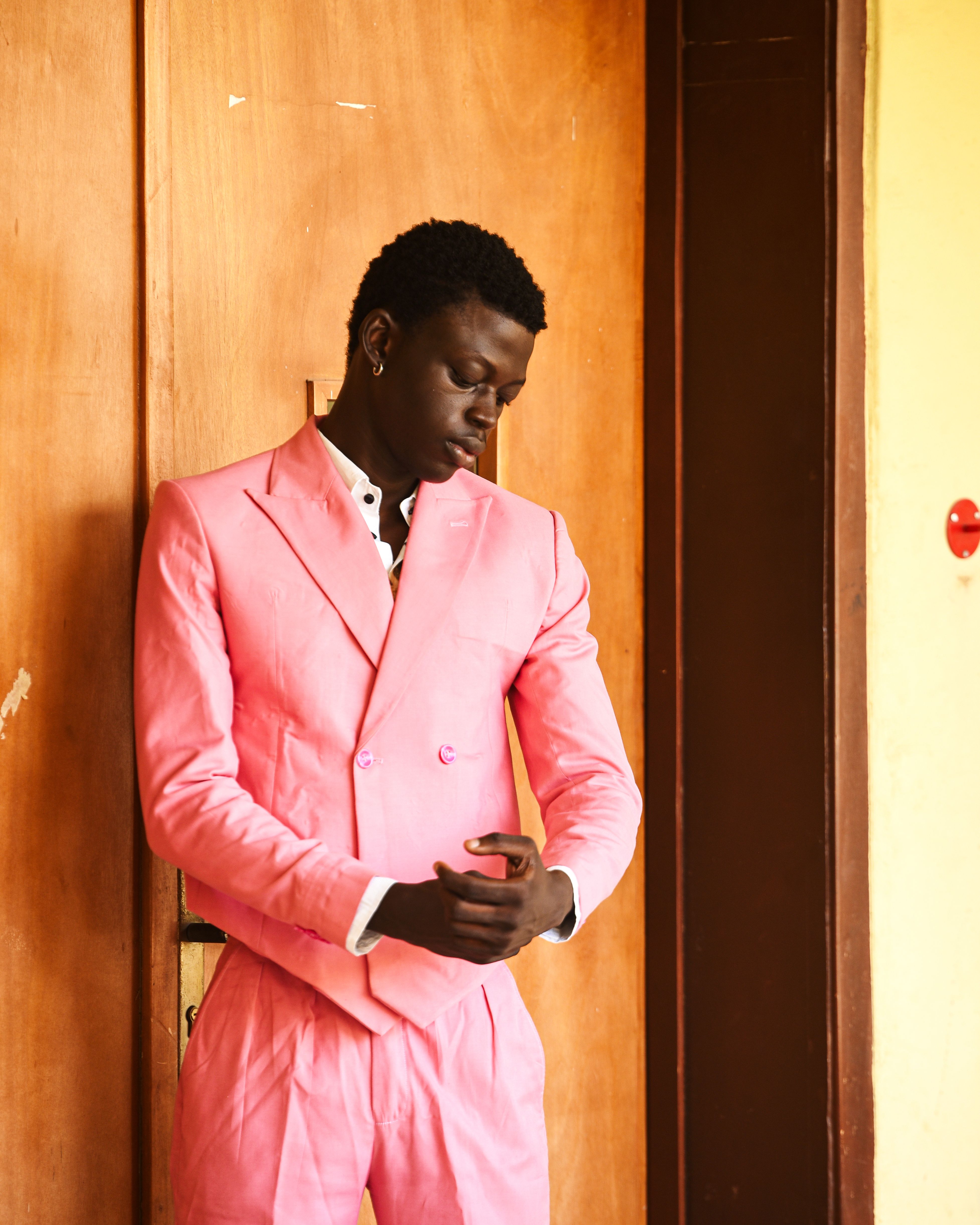 Confident young man wearing a bright pink suit standing against a wooden door.
