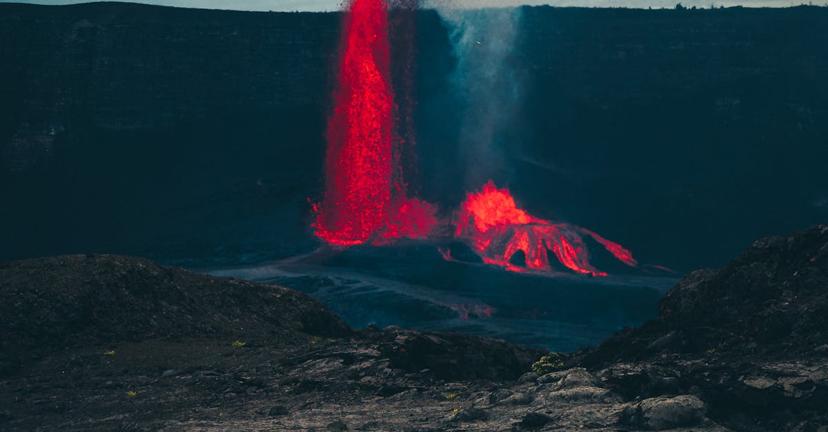 Photo by Michael Li A spectacular view of Kilauea Volcano erupting during twilight, showcasing red lava and smoke against a dark sky.
