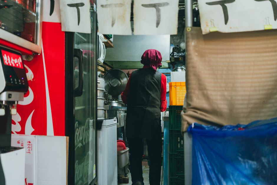 A chef prepares food inside a traditional street food stall in Seoul, reflecting Korean culture.