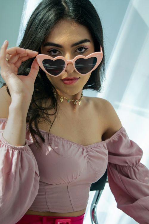 Free Stylish woman in pink top and heart-shaped sunglasses gazing confidently. Stock Photo
