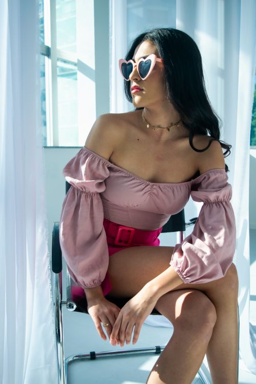 Free Fashionable woman seated indoors wearing pink attire and sunglasses with natural light. Stock Photo