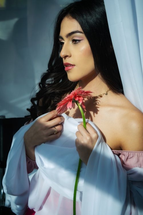 Free Portrait of a young woman holding a flower with serene expression in soft natural light. Stock Photo