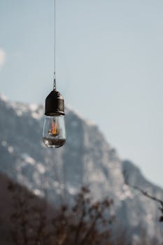 A single light bulb hanging outdoors with a mountainous background, creating a serene and minimalist scene.