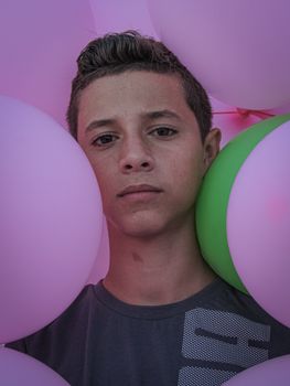 Portrait of a teenager framed by pink and green balloons with a thoughtful expression.