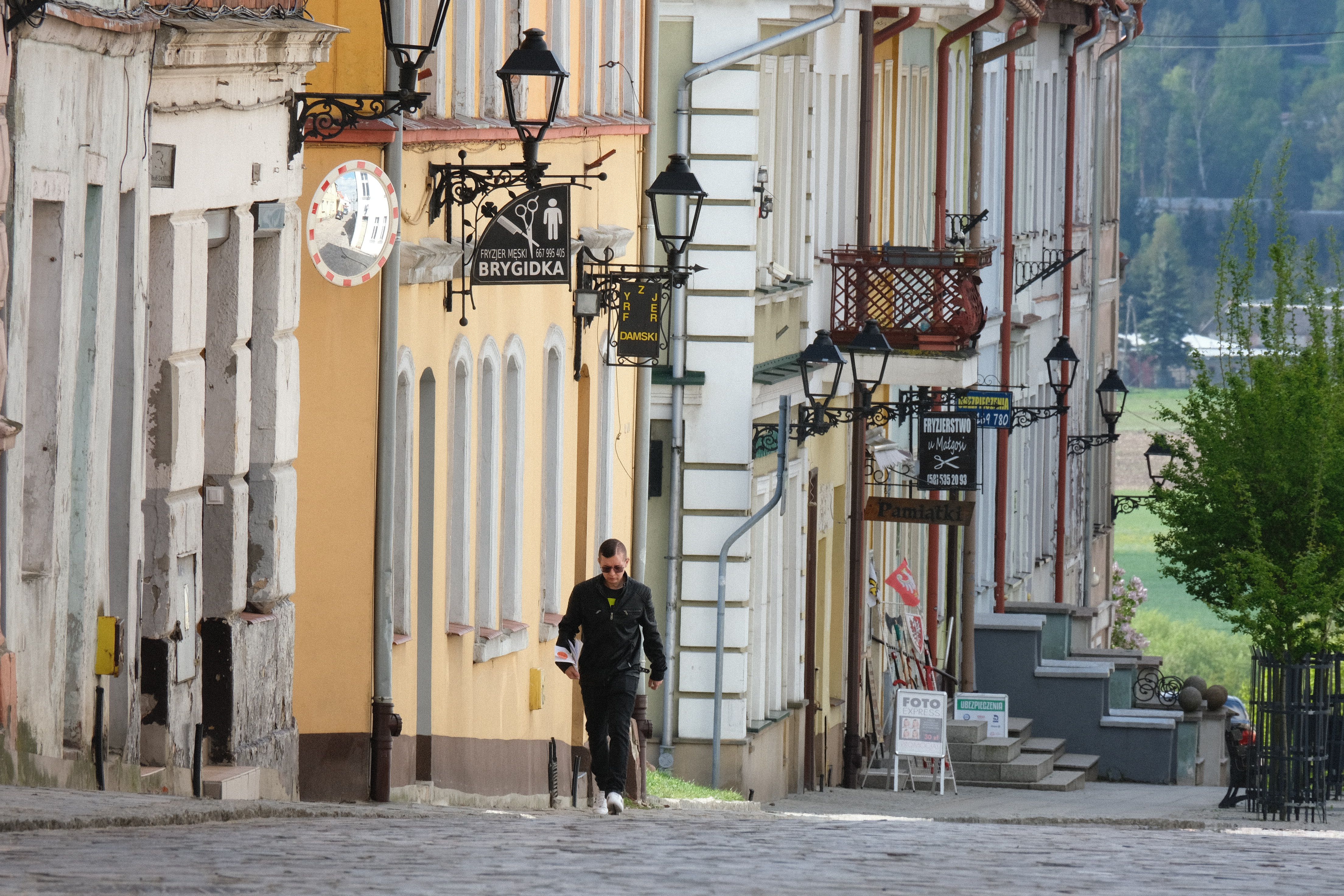 Man walking along a cobblestone street lined with colorful European buildings.
