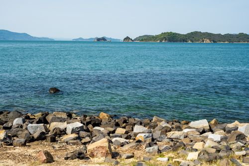 Free A tranquil scene of a rocky coastline overlooking calm blue waters and distant green islands. Stock Photo