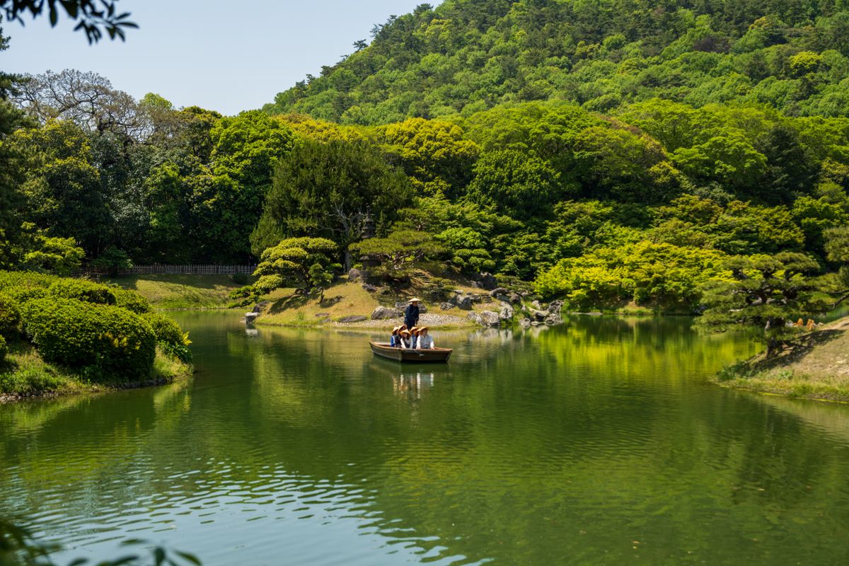 Ritsurin Garden in summer — green landscape with central pond, boat on water, and mountain backdrop