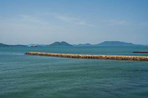 Free Scenic coastal view with mountains and a stone breakwater under a clear blue sky. Stock Photo