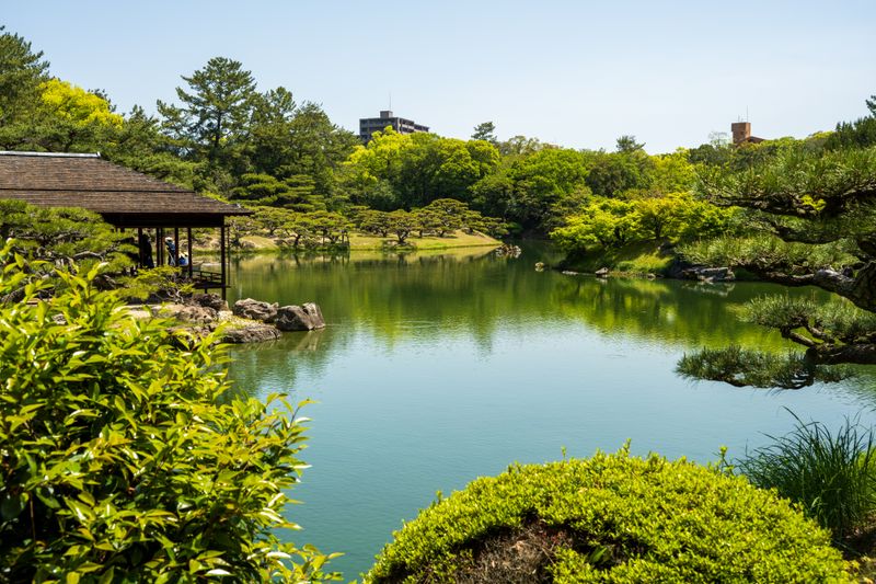 Peaceful Japanese garden scene with a calm pond, lush greenery, and traditional architecture.