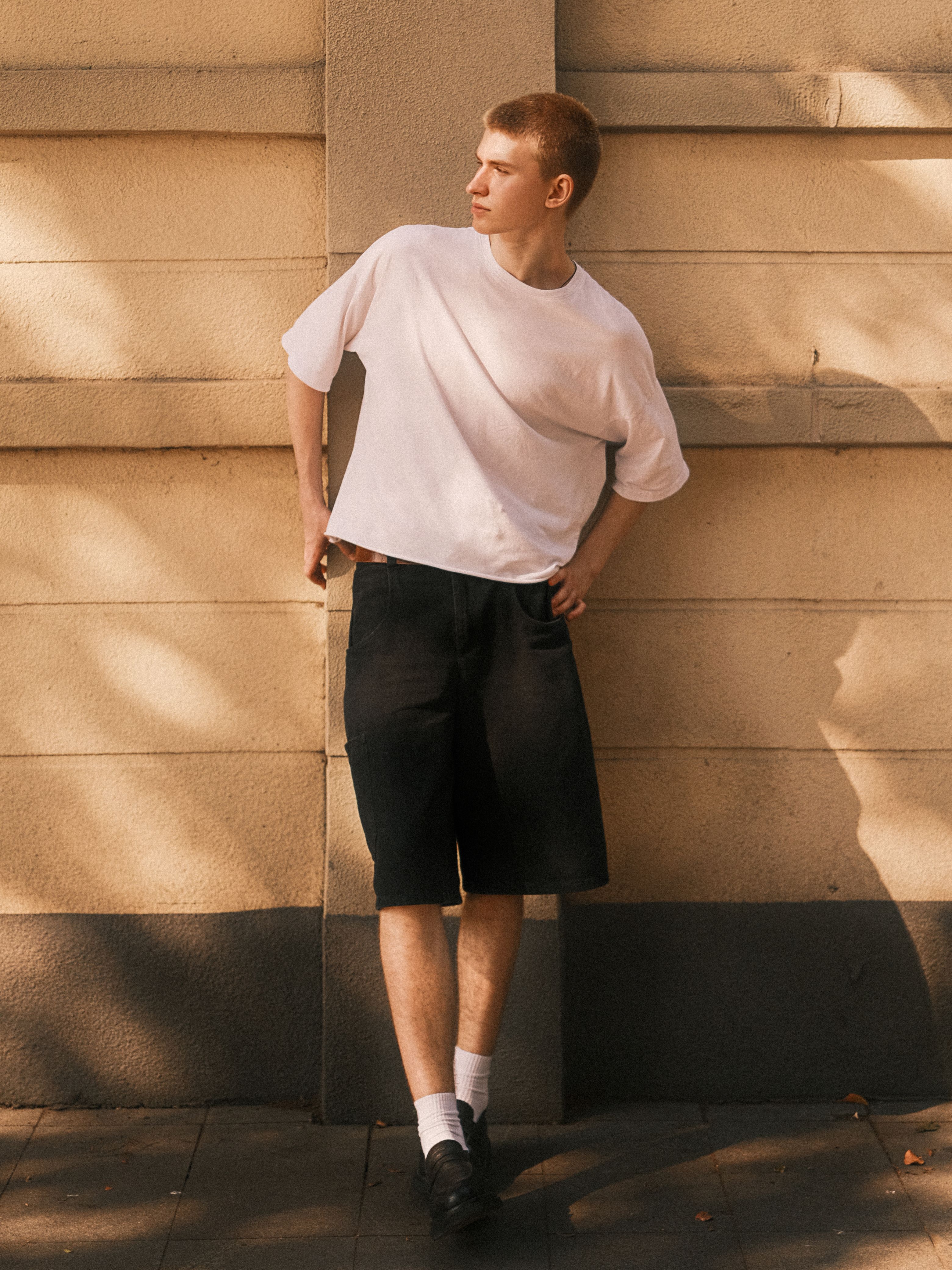 Young man in casual attire leaning against a city wall, showcasing urban street style.