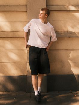 Young man in casual attire leaning against a city wall, showcasing urban street style.