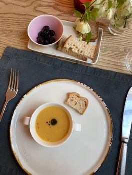 Overhead view of a stylish table setting with soup, bread, and olives.