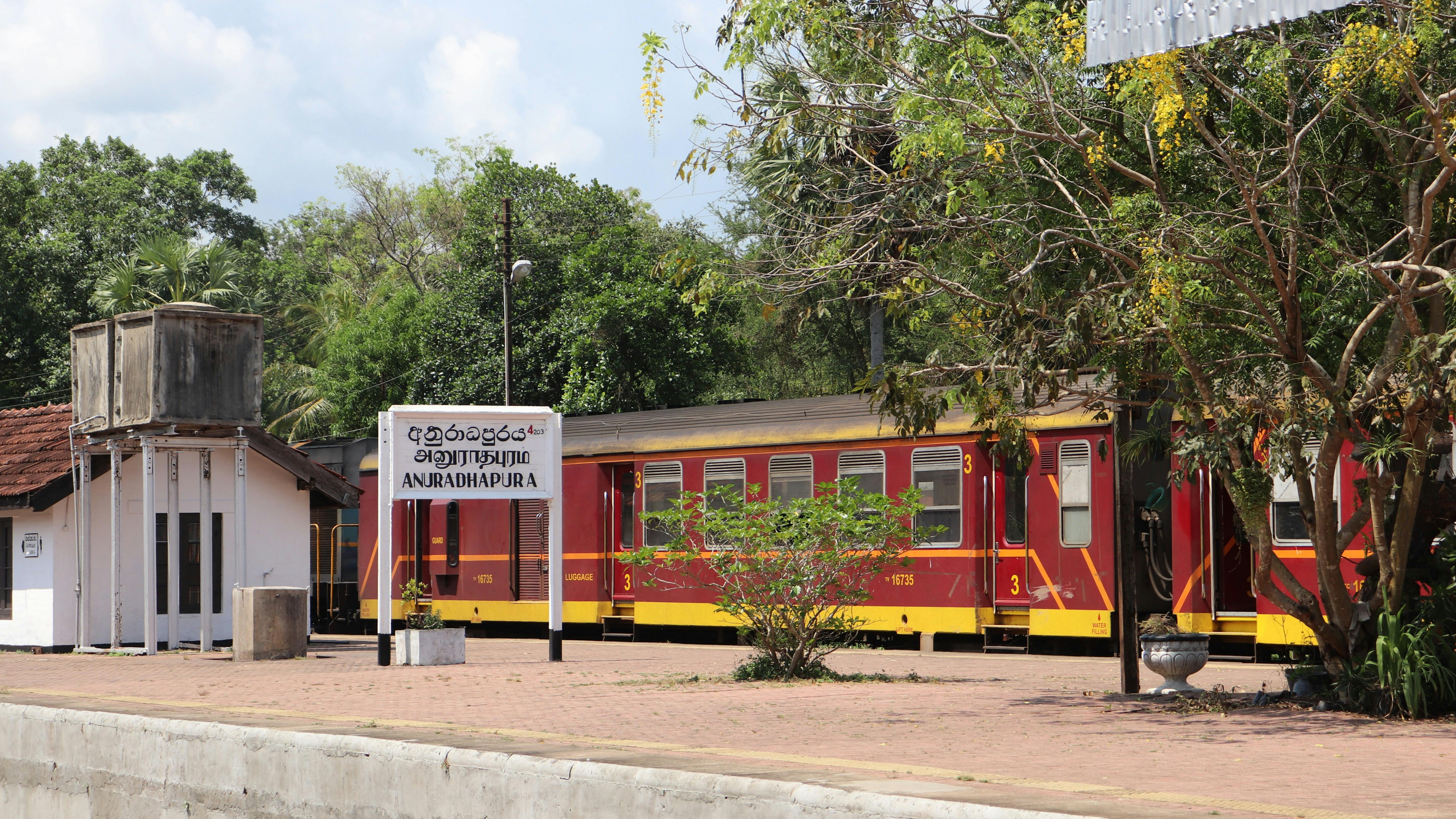 Un train rouge à la gare d'Anuradhapura avec des environs verdoyants à la destination.