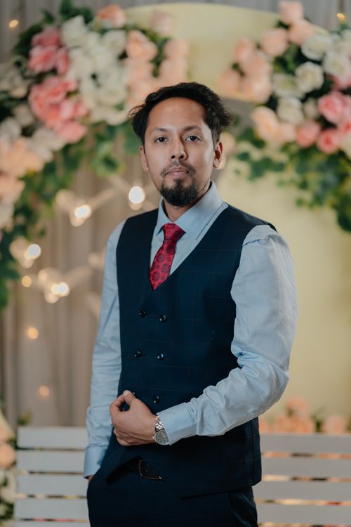 Free A sophisticated man in formal attire, standing against a floral backdrop with soft lighting. Stock Photo