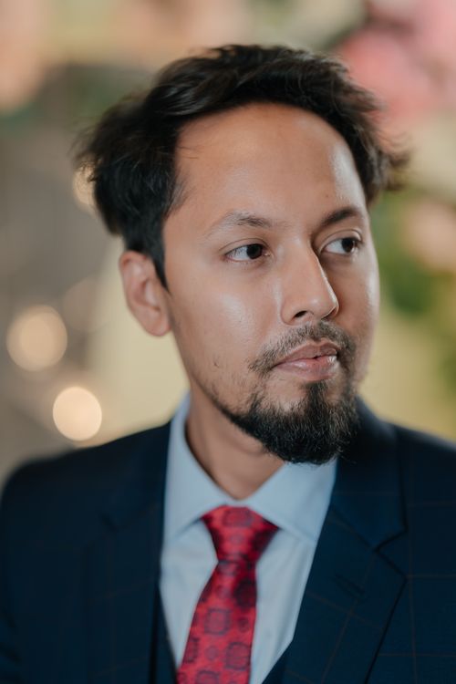 Free A contemplative man in a dark blue suit with a red tie, set against a blurred background of warm lights. Stock Photo