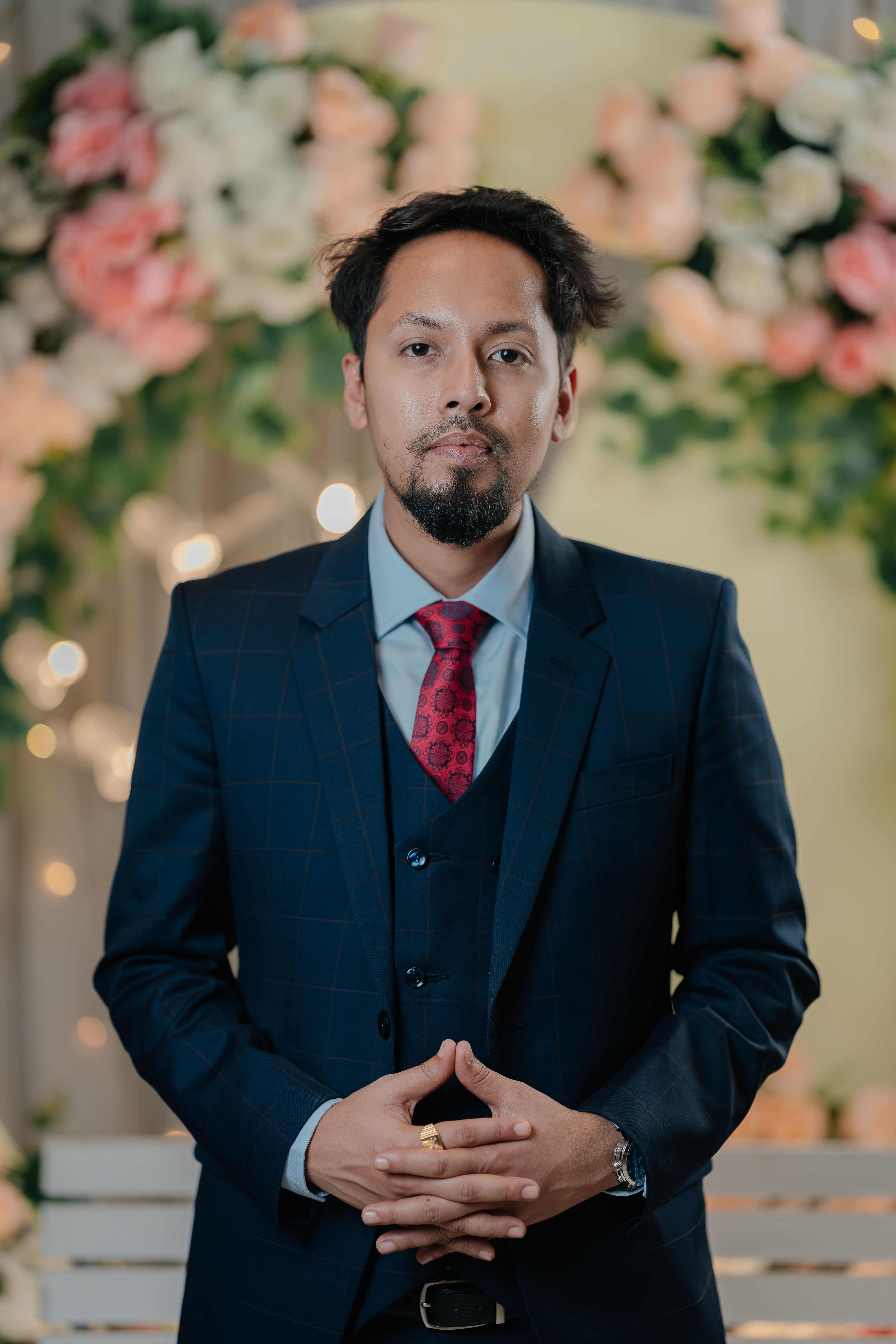 Young man in a suit standing in front of a floral arrangement, exuding confidence and style.