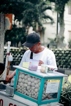 Street vendor selling traditional snacks in a historic square of Jawa Barat, Indonesia.