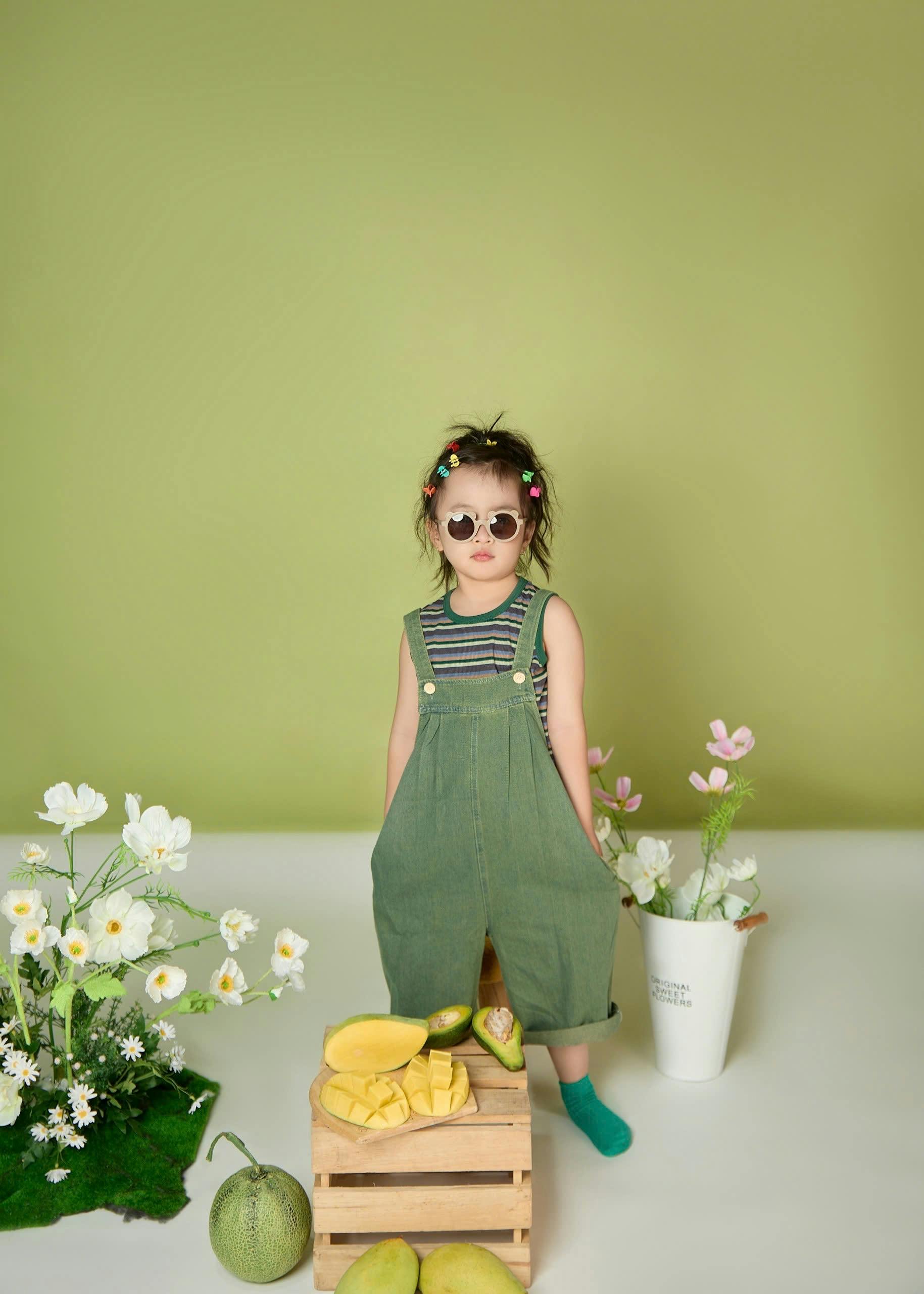 bezplatná Rozkošné dítě v zelených overalech se slunečními brýlemi v hravém prostředí. Základová fotografie