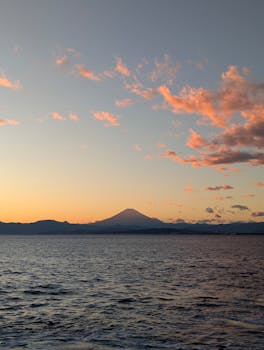 A breathtaking sunset view of Mount Fuji from Fujisawa with pink clouds and a tranquil sea nearby.
