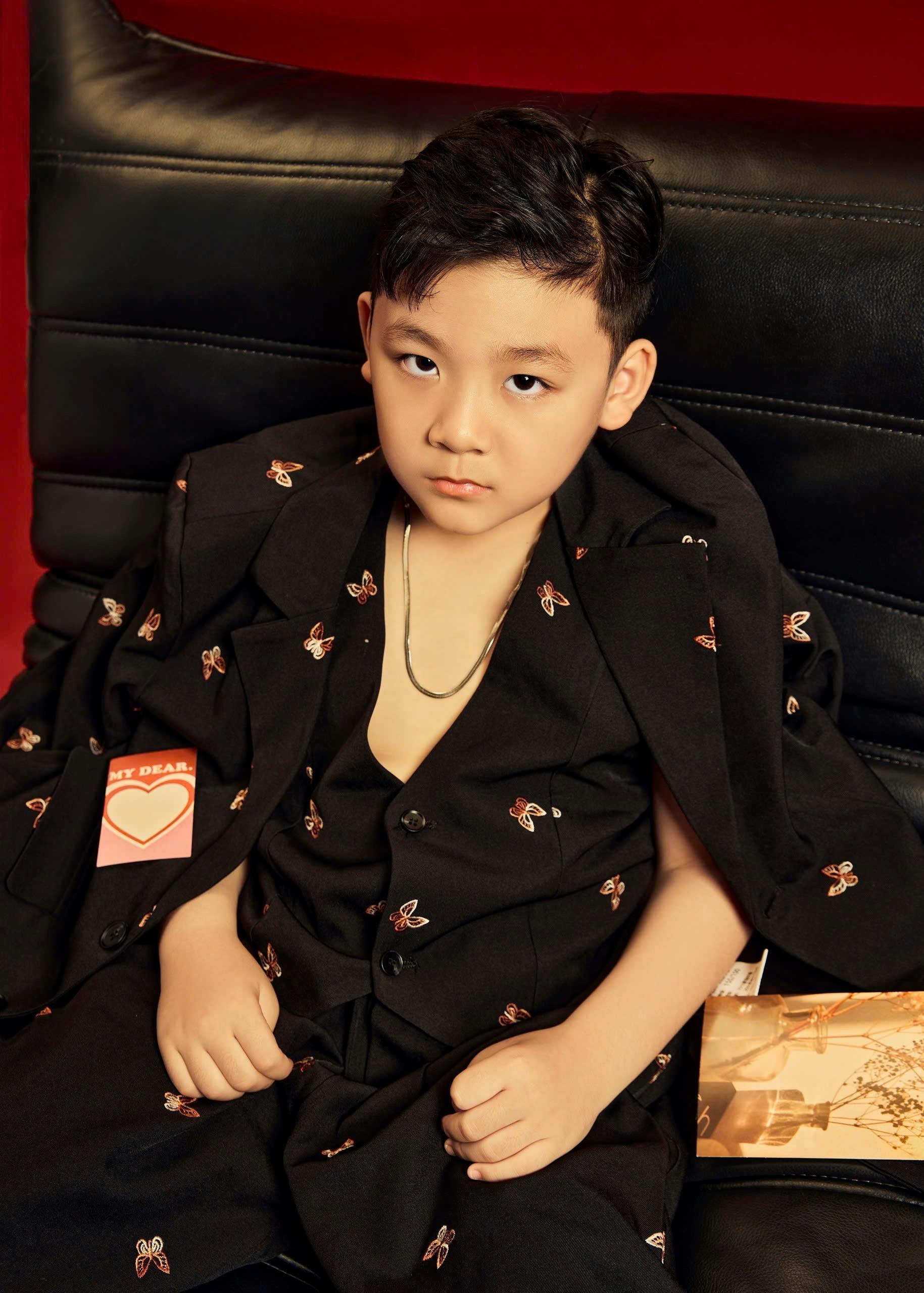 Free Stylish young boy in an elegant black suit poses confidently on a leather chair indoors. Stock Photo