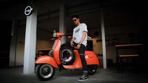 Young man posing with a classic Vespa scooter inside a trendy Bangkalan cafe.