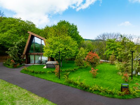 Modern A-frame chalet surrounded by lush greenery and vibrant flowers, perfect for eco-tourism.