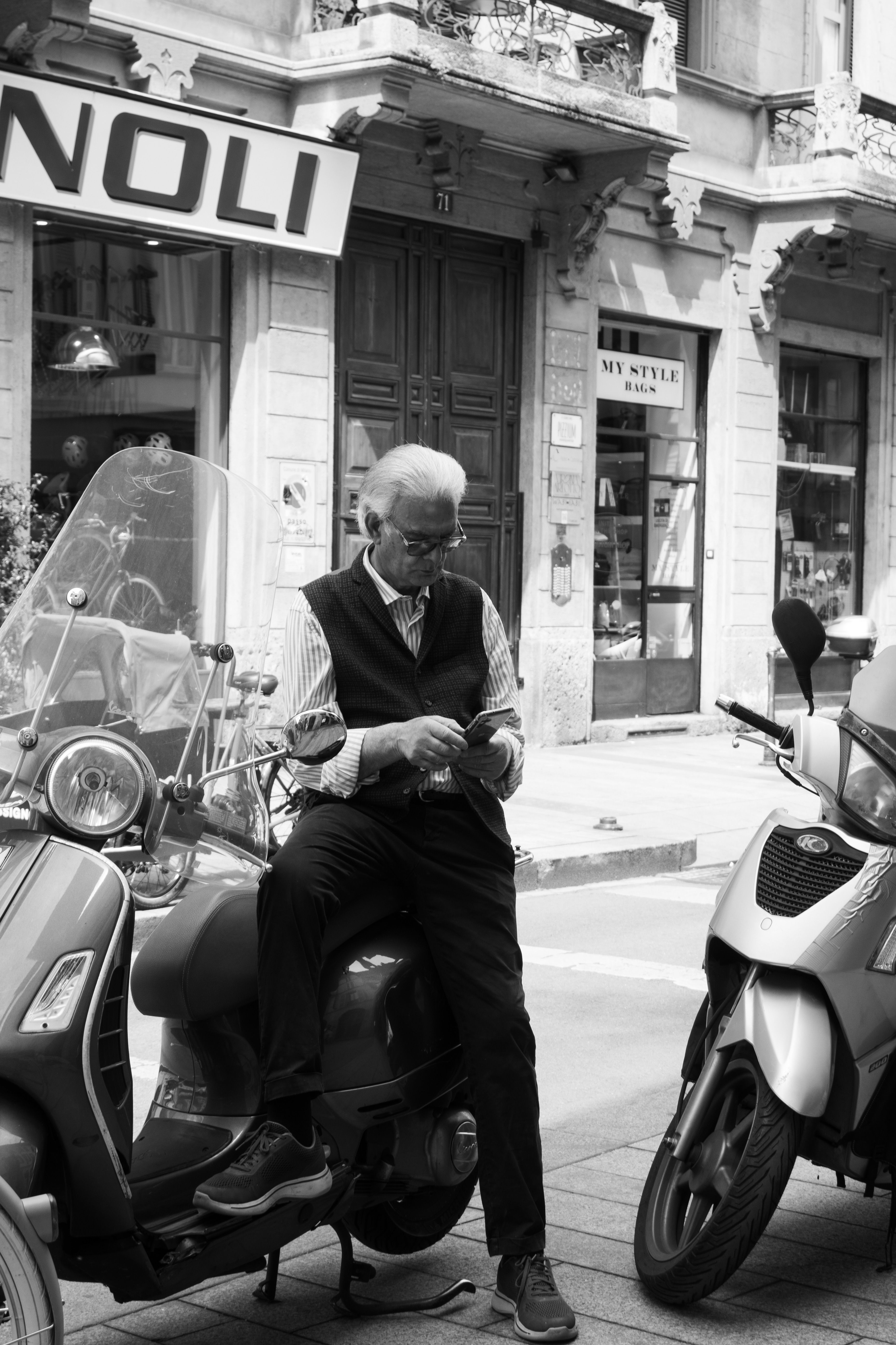 Stylish older man in Milan leaning on a scooter on a classic city street.