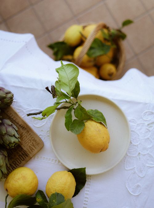 Free Top view of fresh lemons on white linen with basket and artichokes outdoors. Stock Photo