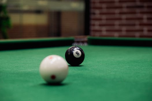 Focused shot of a black eight ball and a white cue ball on a pool table indoors.