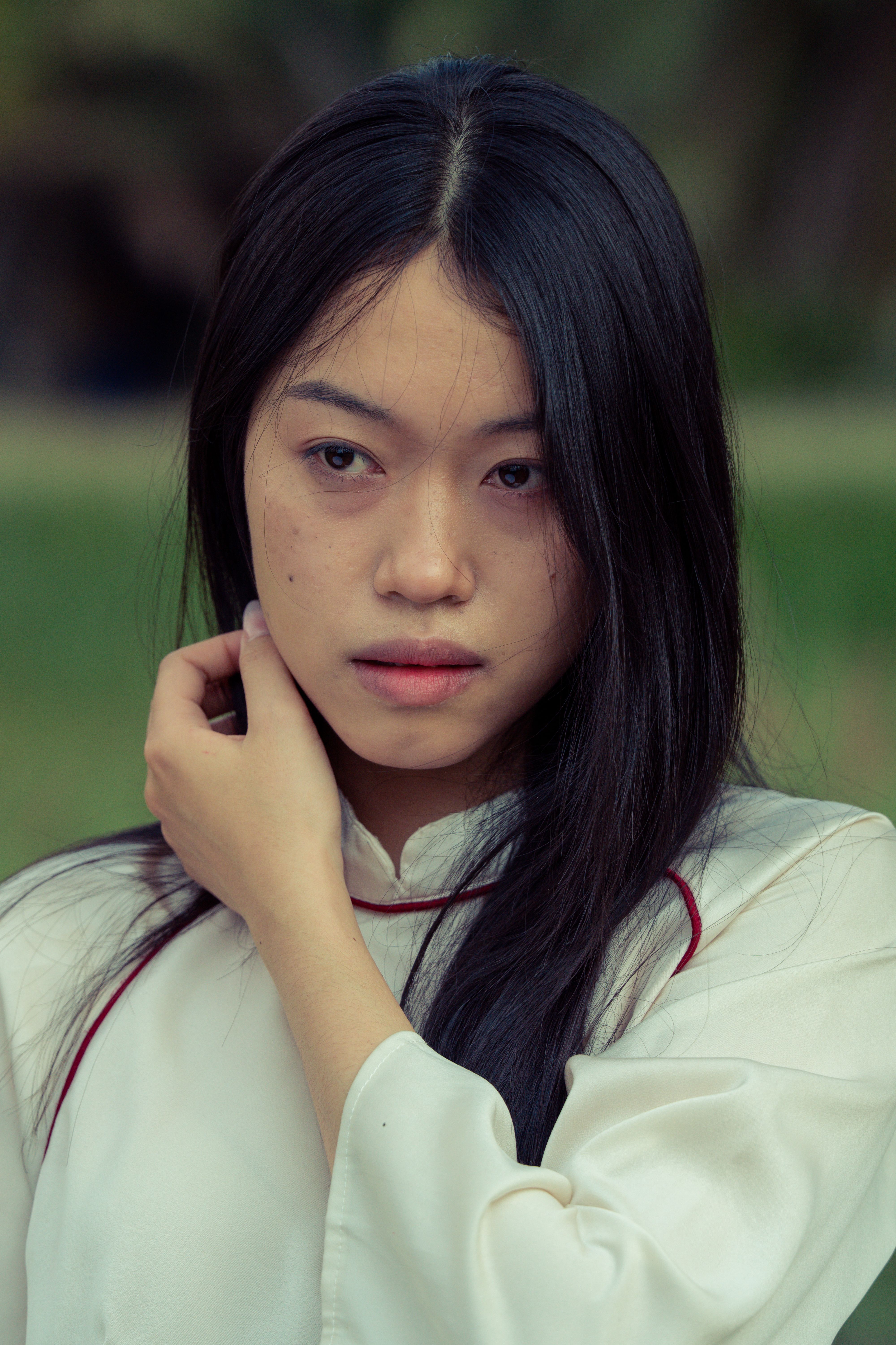 Young woman in a white blouse looking contemplative outdoors.