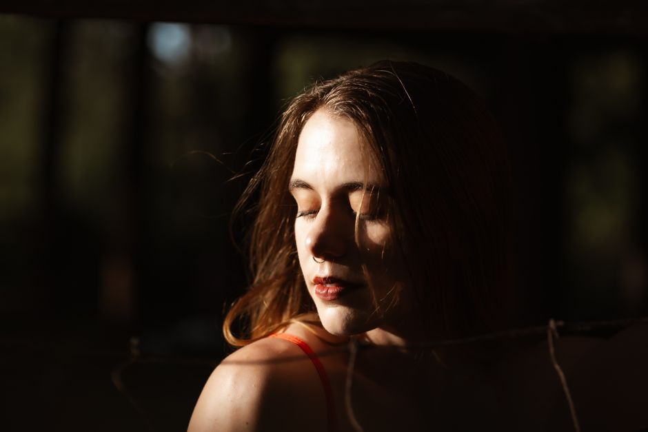 A peaceful portrait of a Caucasian woman with closed eyes, bathing in sunlight outdoors.