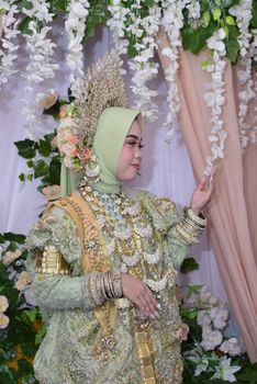 Bugis bride wearing elaborate traditional wedding attire with intricate details and floral backdrop. - Fotografer Sidoarjo