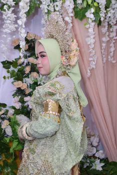 Bride in ornate traditional Bugis attire with intricate floral backdrop. - Fotografer Sidoarjo