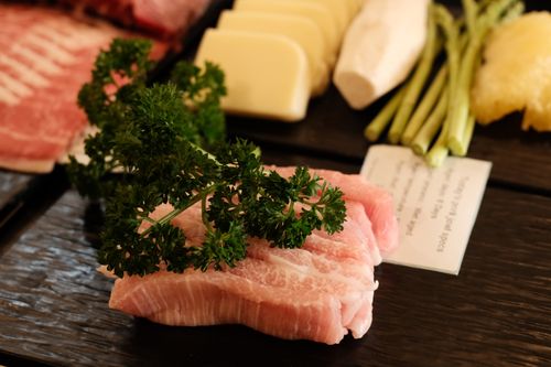 Free A close-up of raw meat with parsley and an assortment of vegetables on a black tray, ideal for cooking. Stock Photo