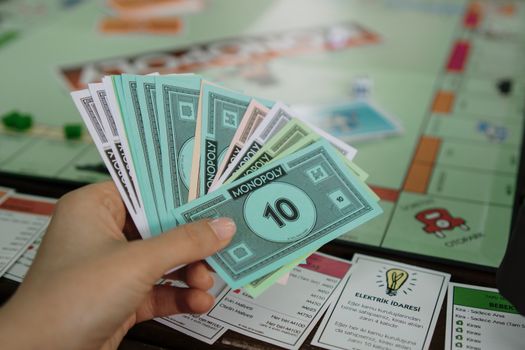 Hand holding colorful Monopoly money over a game board, symbolizing strategy and play.