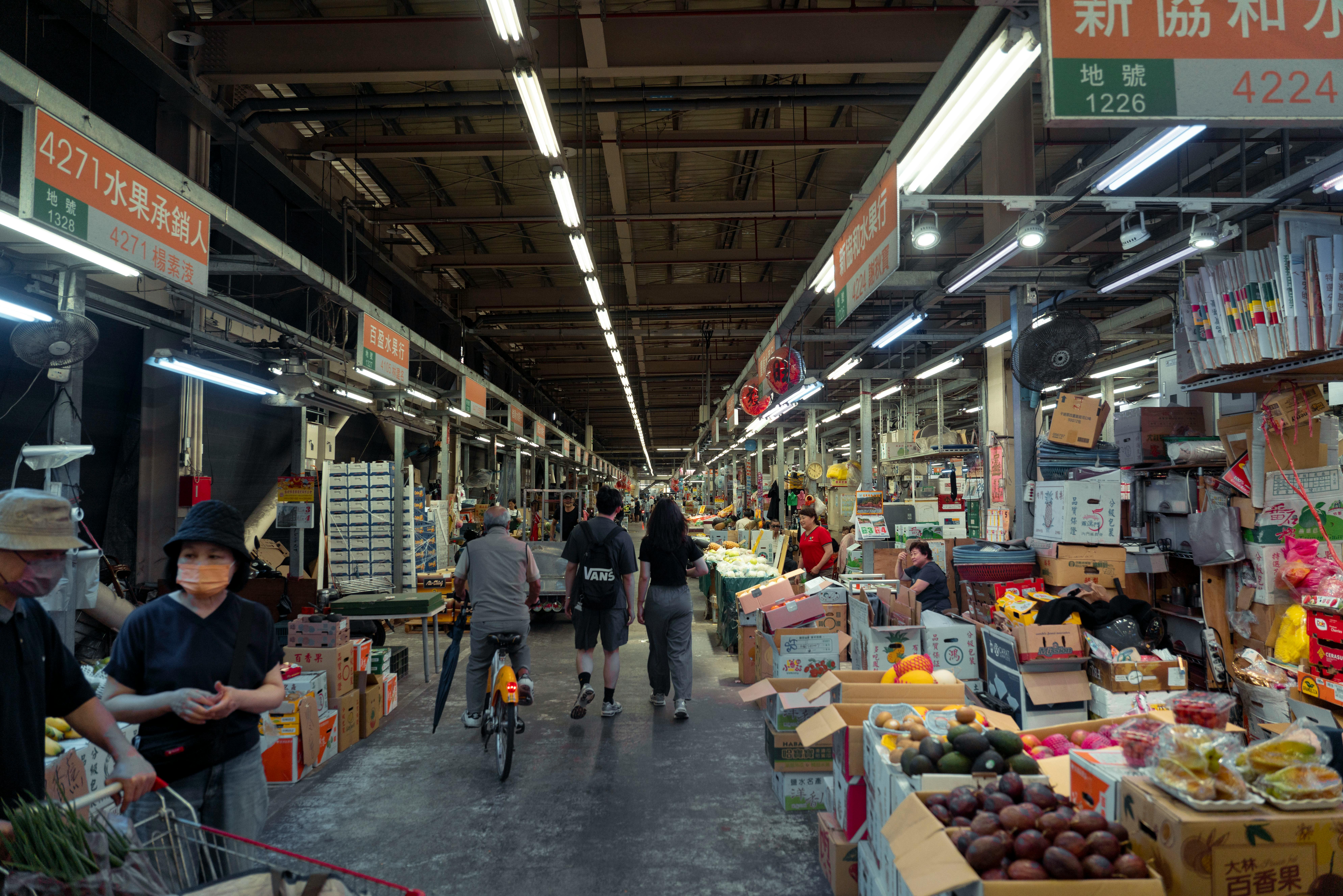 Indoor street market with diverse people and fresh produce displays in an Asian setting.