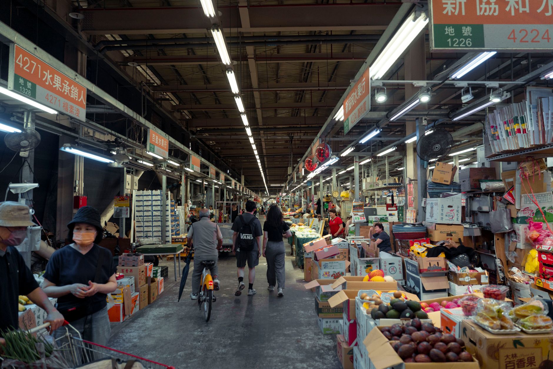 Indoor street market with diverse people and fresh produce displays in an Asian setting.
