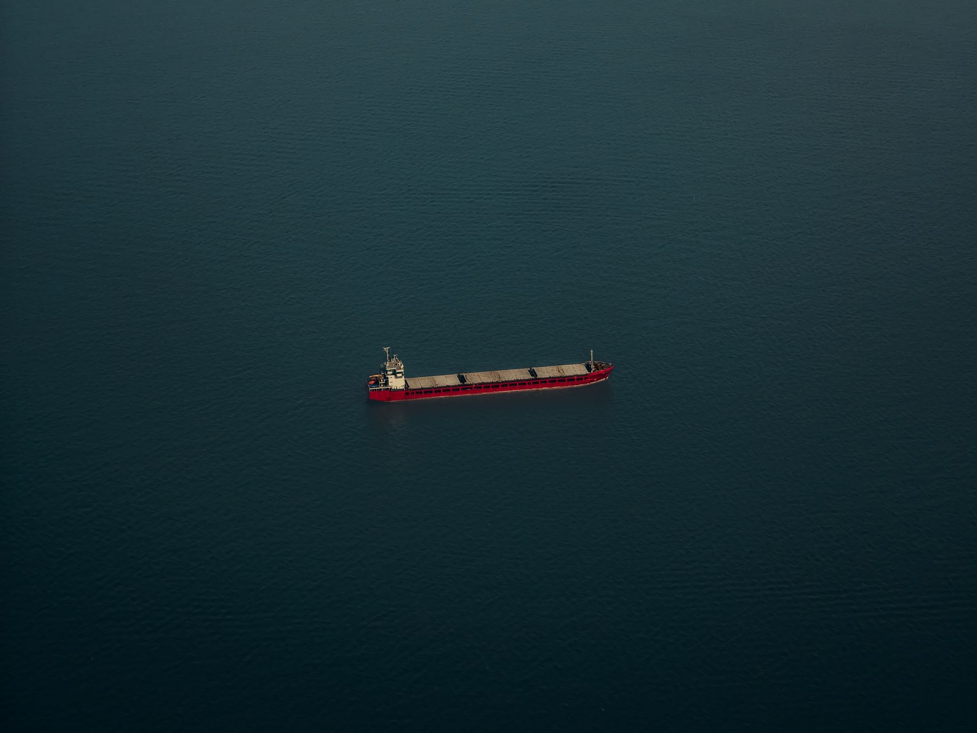 A lone cargo ship crossing open, deep-blue ocean under a clear sky