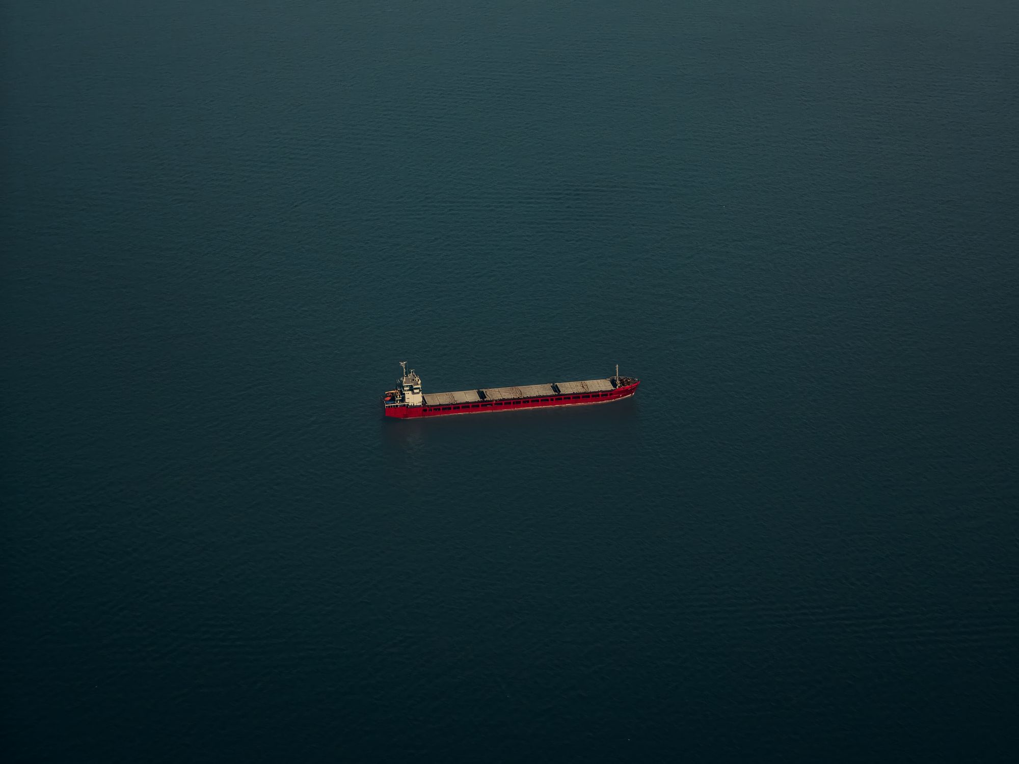 A lone cargo ship navigates the vast, serene expanse of the ocean under clear skies.