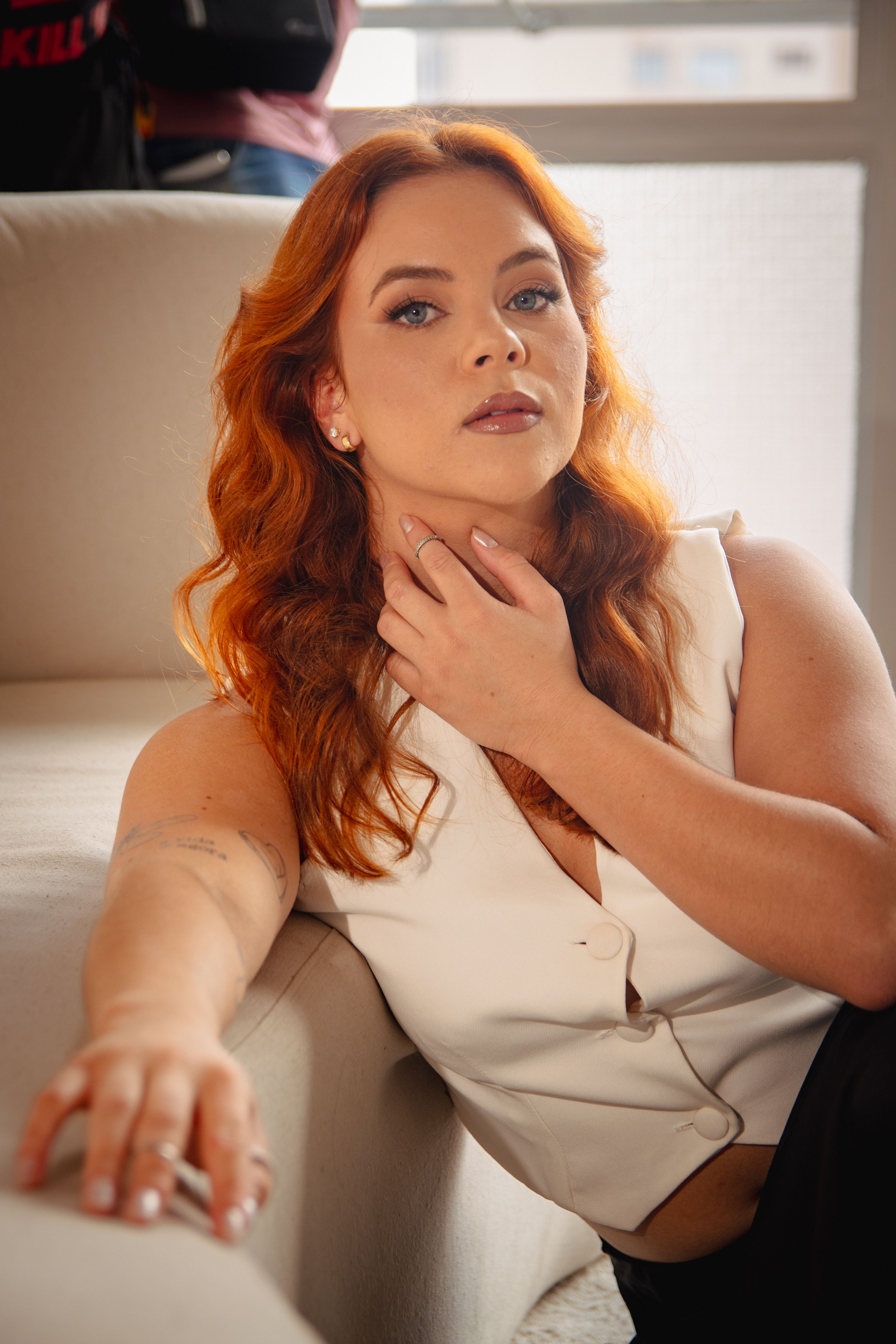 Young woman with red hair sitting thoughtfully indoors, showcasing modern style.