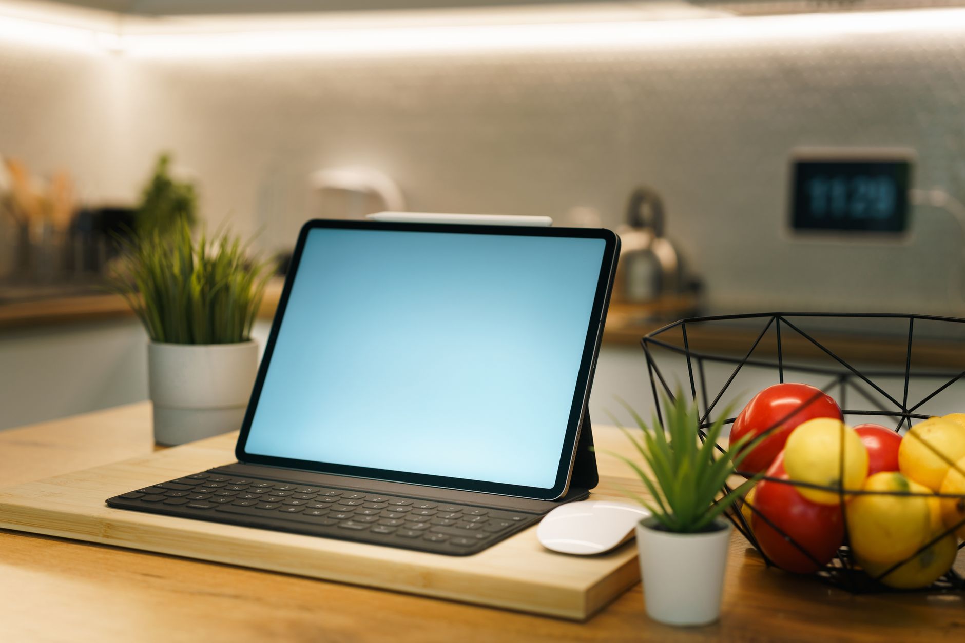 Sleek tablet in a cozy home kitchen with plants and fresh fruits for a productive workspace.