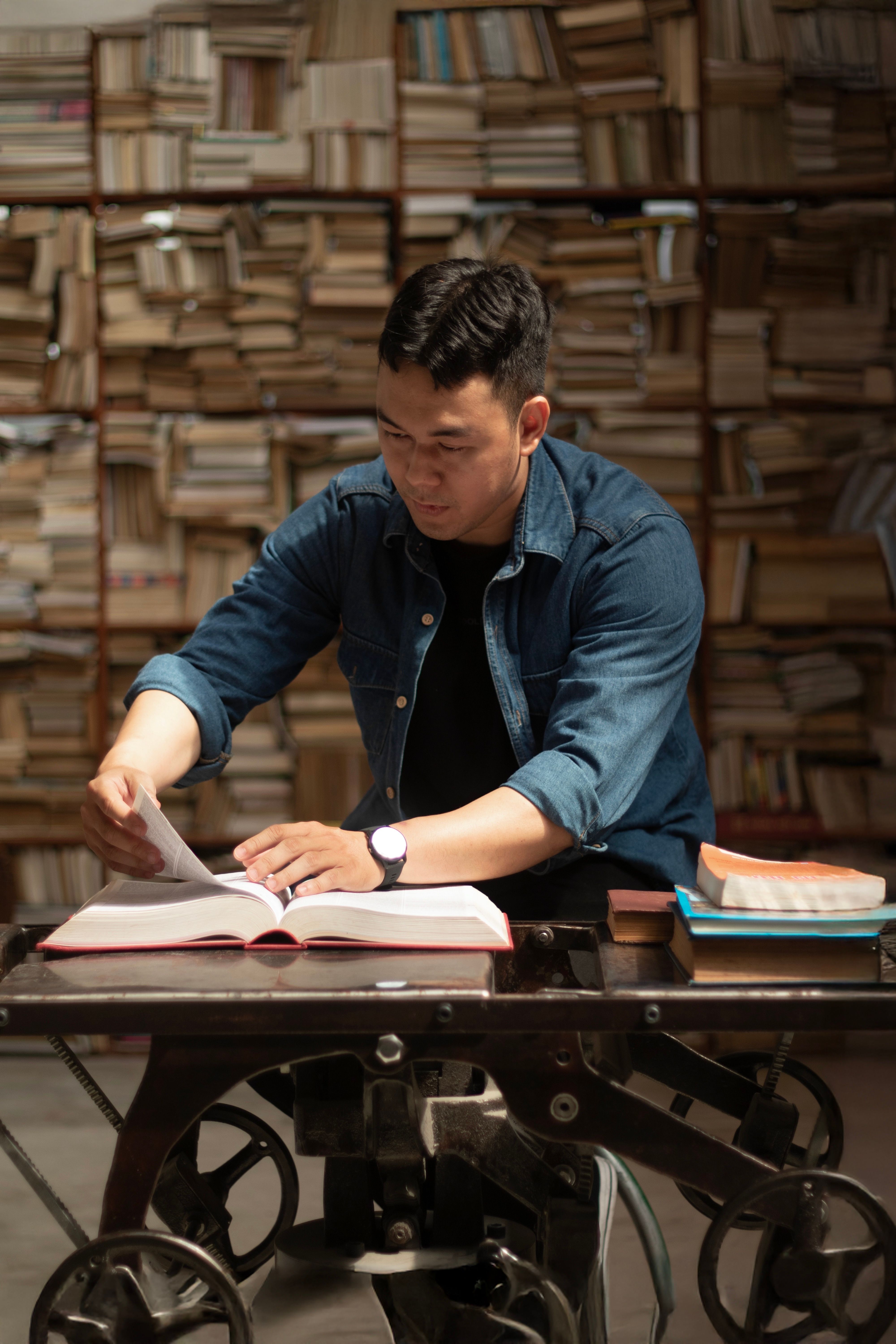 Man reading a book in a cozy library with a wall of books behind him.