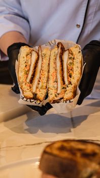 Chef presenting a delicious homemade chicken sandwich cut in half, showcasing fresh ingredients.