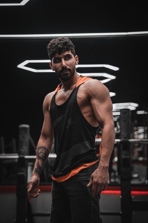 Free Fit man in gym showcasing muscles wearing black tank top. Modern interior. Stock Photo