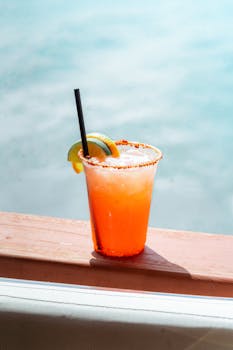 A vibrant tropical margarita garnished with lime and chili, set against a sunny coastal background.