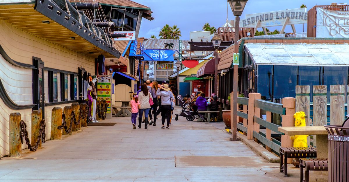 Families stroll along the colorful Redondo Beach Pier under a clear sky in California.